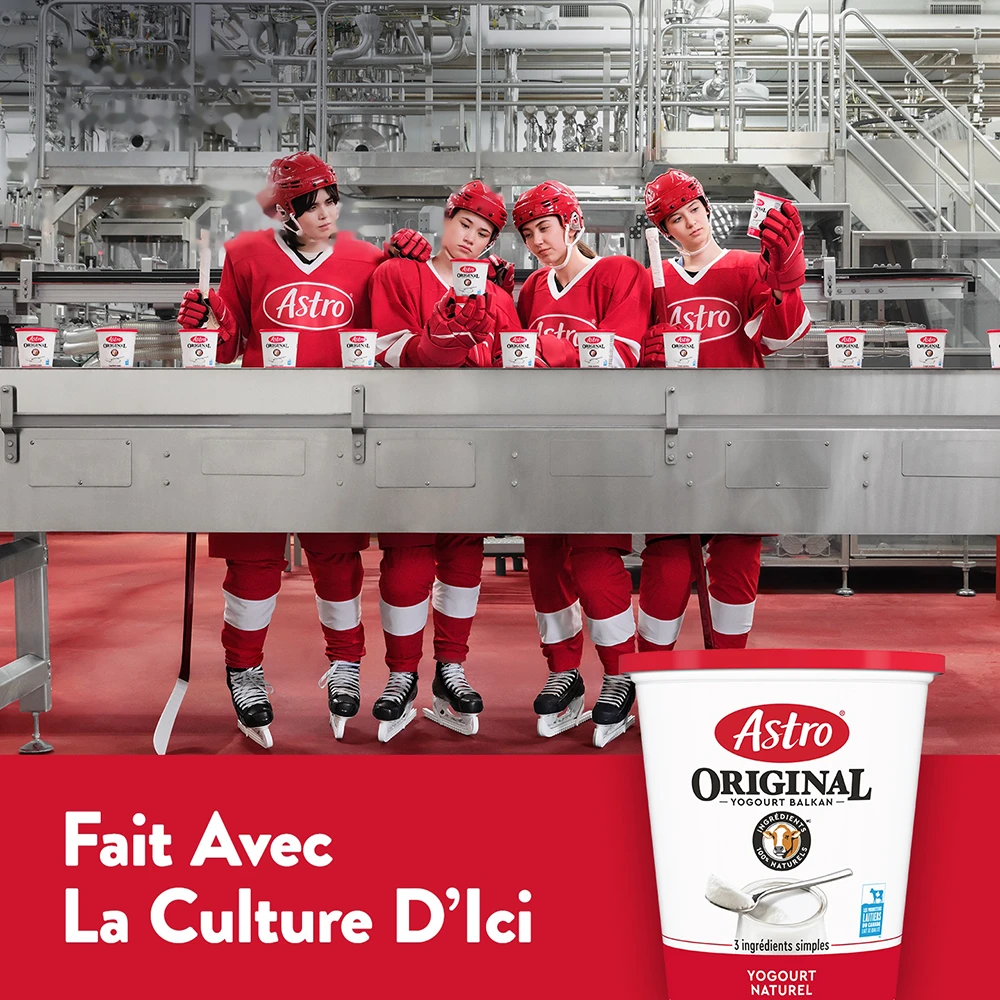 De jeunes joueuses de hockey en rouge derrière un convoyeur rempli de pots de yogourt Astro Original.