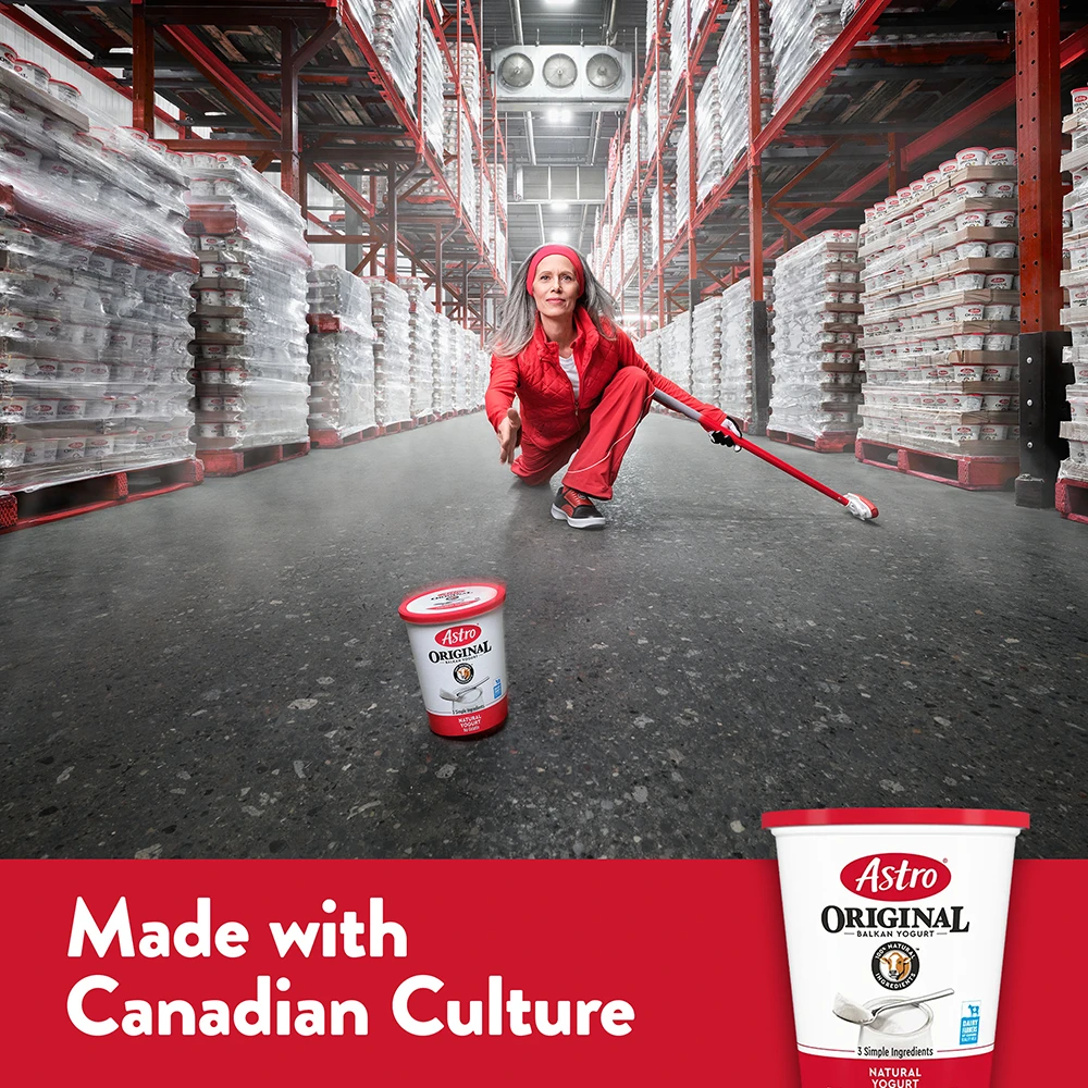 A curler in red crouches mid-throw, sliding a tub of Astro Original yogurt down a warehouse aisle.