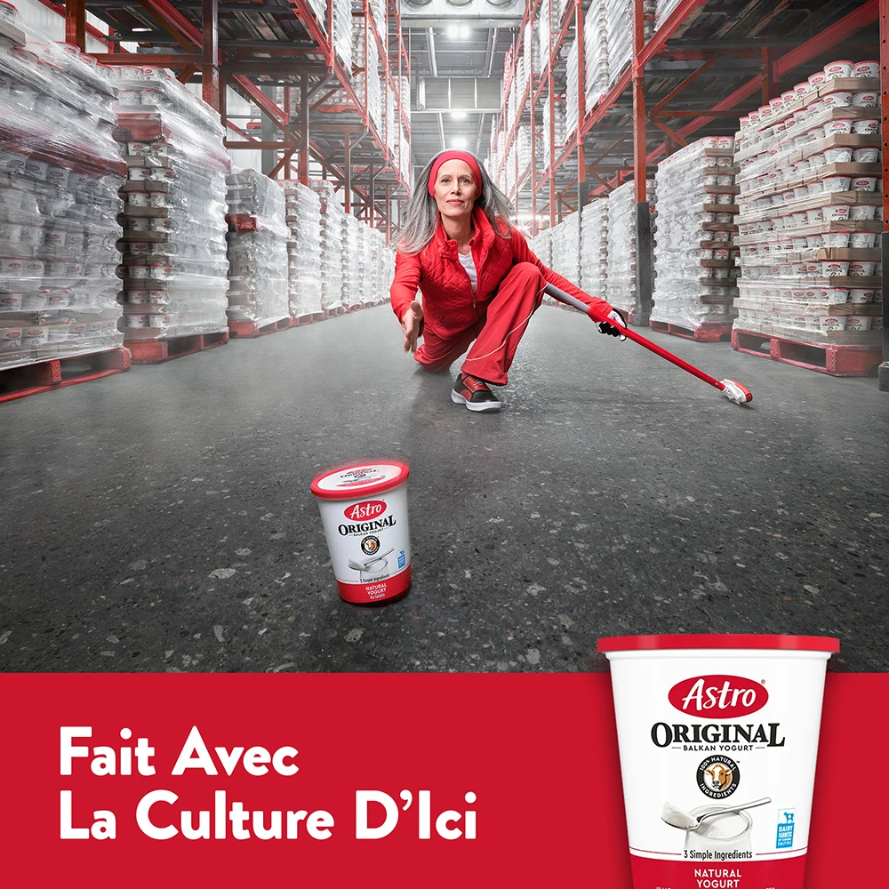 Une curleuse en rouge lance un pot de yogourt Astro Original dans une allée d’entrepôt.