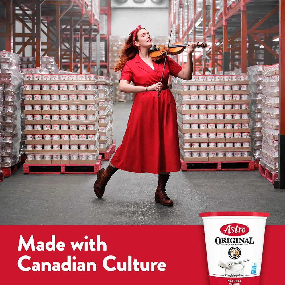 A fiddler in a red dress plays the violin between pallets of Astro Original yogurt.