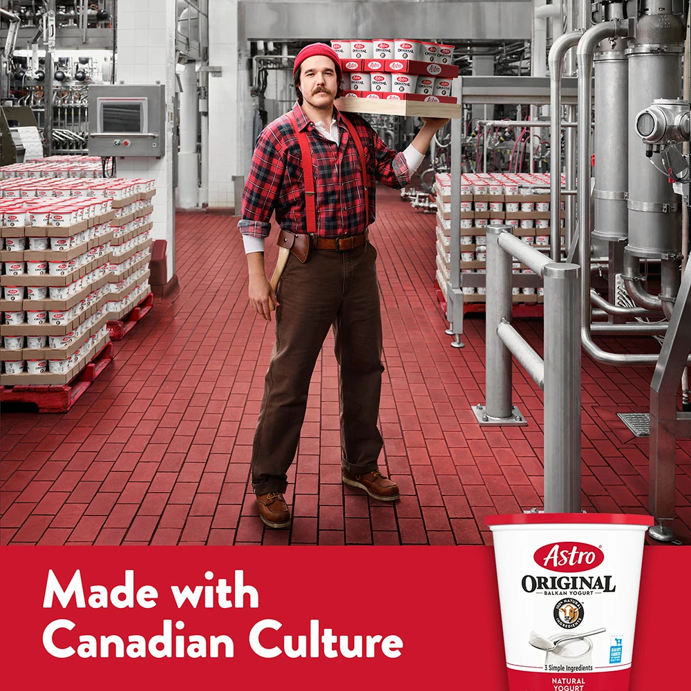 A lumberjack in red plaid carries a tray of Astro Original yogurt tubs through the factory.