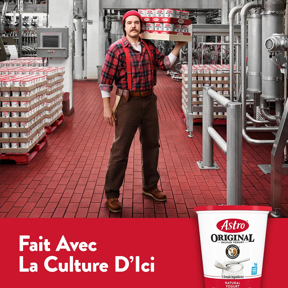 Un bûcheron en chemise à carreaux rouge transporte un plateau de pots de yogourt Astro Original dans l’usine.